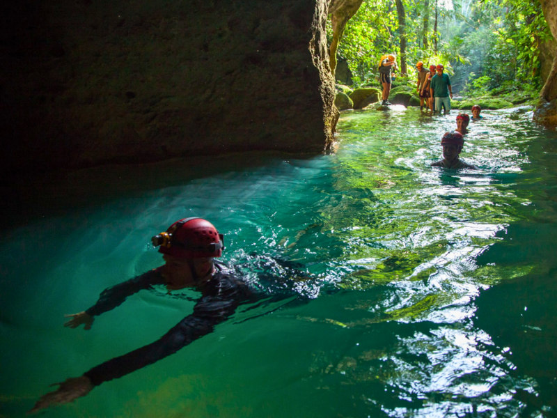 People swimming in a clear, turquoise pool with rocky walls and greenery; ATM caves, Actun Tunichil Muknal, Cayo, Belize