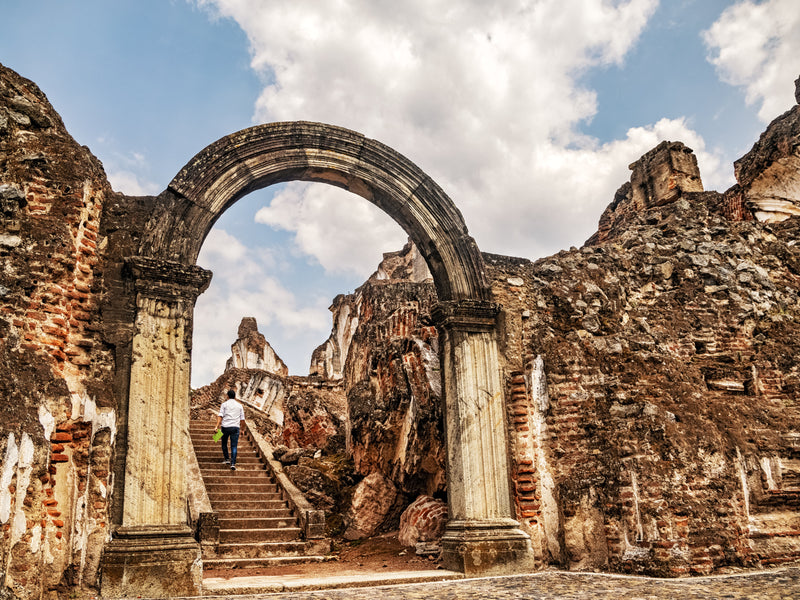 Ruins of an ancient building with archway and columns under a blue sky with clouds; Antigua, Guatemala, La Recoleccion