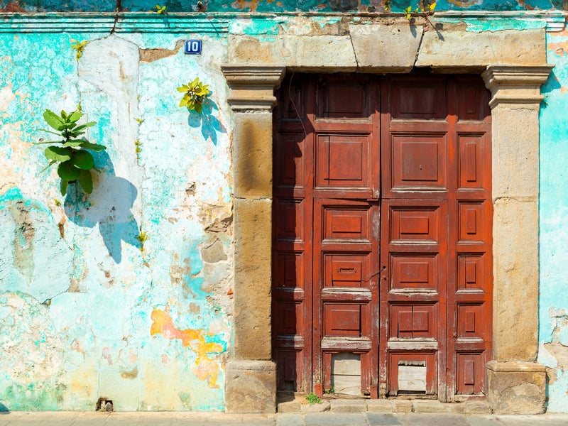 Old building with a wooden door and peeling multicolored wall; Antigua, Guatemala