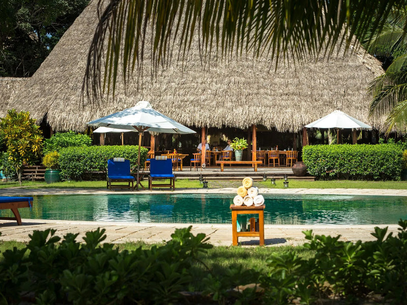 Pool area with thatched-roof building, chairs, and tables in a tropical setting; Turtle Inn, Placencia, Belize