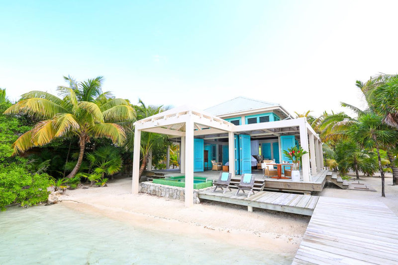 Turquoise villa with a wooden deck and surrounding palm trees on a clear day; Cayo Espanto private island villa