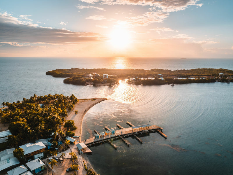 Sunset over a coastal area with a dock and houses; Placencia peninsula, Belize aerial view