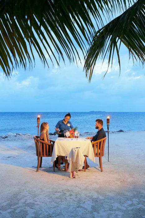 People dining on a sandy beach with ocean view and palm trees; Ray Caye private dining, Belize portrait