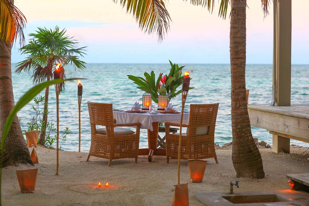Beachside dining setup with tables, chairs, and candles by the ocean; Cayo Espanto Belize private island