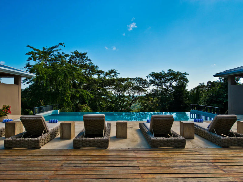 Outdoor seating area with lounge chairs around a pool, surrounded by trees and clear blue sky; Copal Tree Lodge, Punta Gorda, Belize