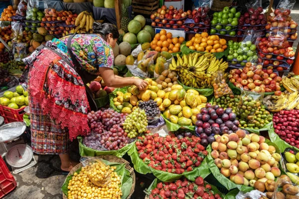 Woman shopping at a vibrant fruit market with a variety of fruits displayed, Antigua, Guatemala