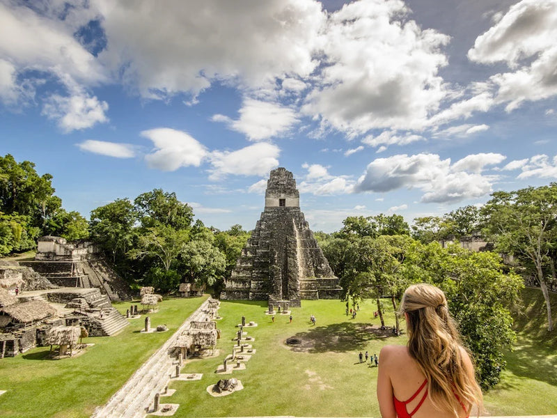 Woman overlooking ancient Mayan ruins with lush greenery and blue sky; Tikal, Peten, Guatemala