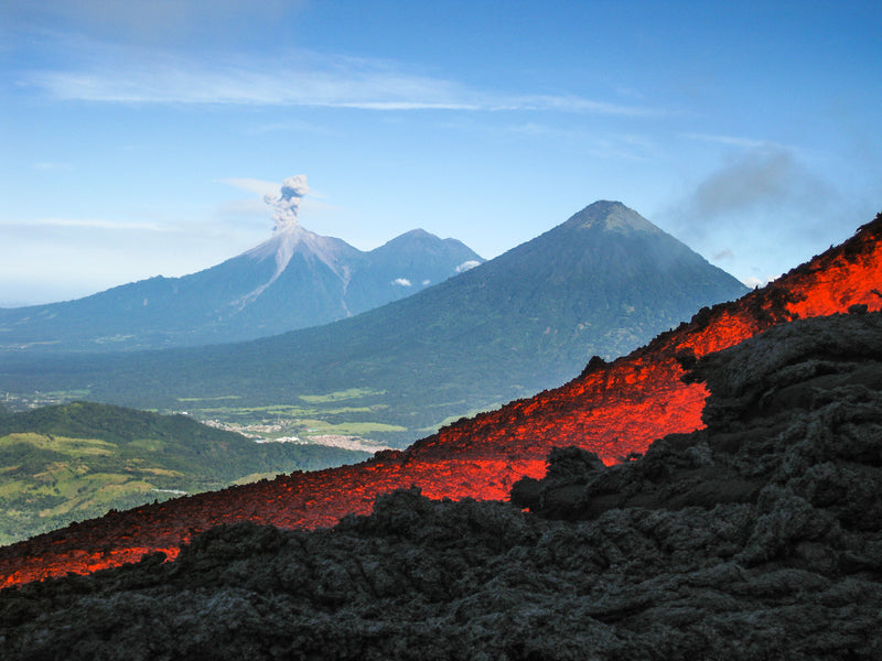 Volcanic landscape with glowing red lava and distant mountains under a blue sky. Pacaya, Valley of the Volcanoes, Guatemala.