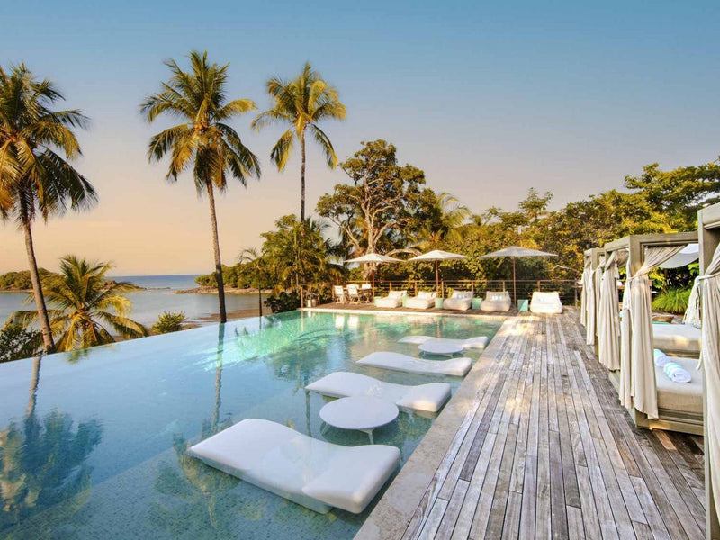 Infinity pool with lounge chairs and palm trees by a body of water. Islas Secas, Panama.