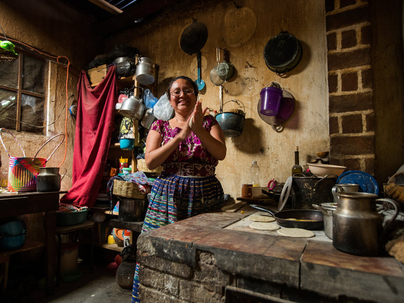 Woman in a rustic kitchen with pots and pans hanging on the wall; Guatemala San Pedro La Laguna