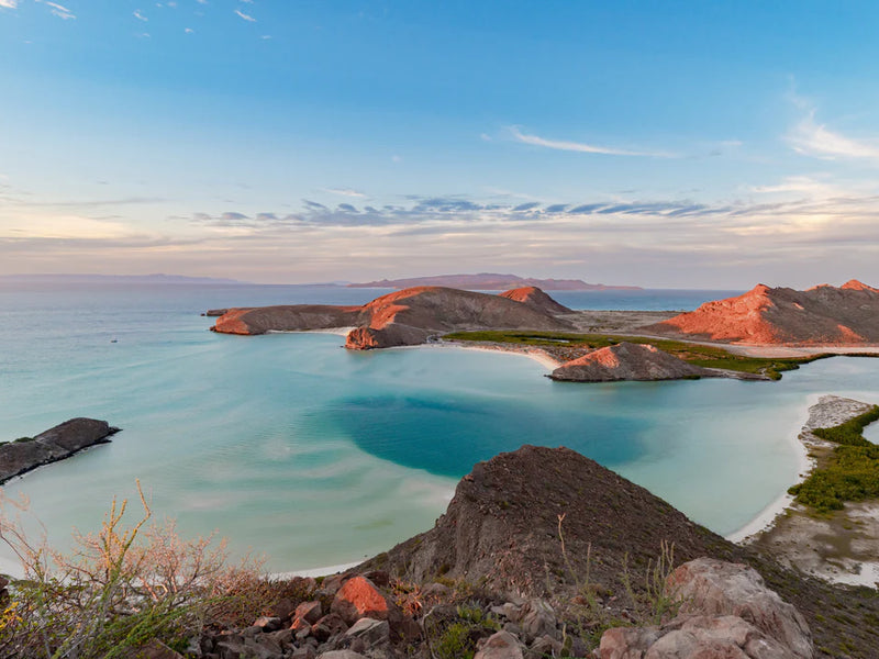 Scenic view of a lagoon surrounded by rocky islands with clear blue water and a bright sky. Balandra, Baja California, Mexico.