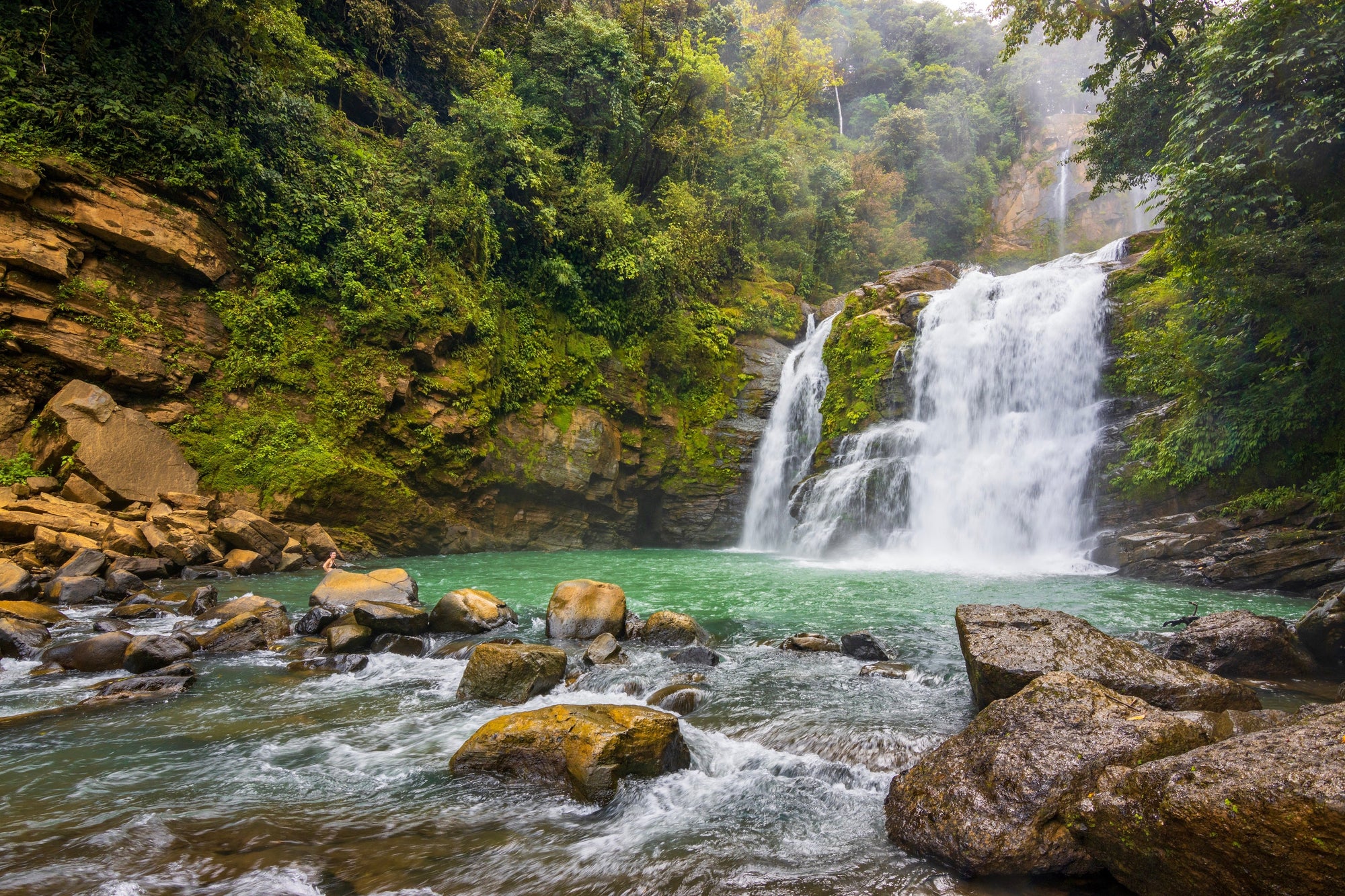 Waterfall in a lush green forest with rocks and water flowing; Nauyaca Falls Dominical Costa Rica