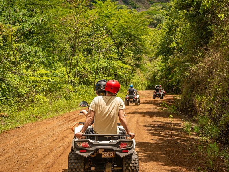 People riding ATVs on a dirt road through a forest; Nosara, Costa Rica