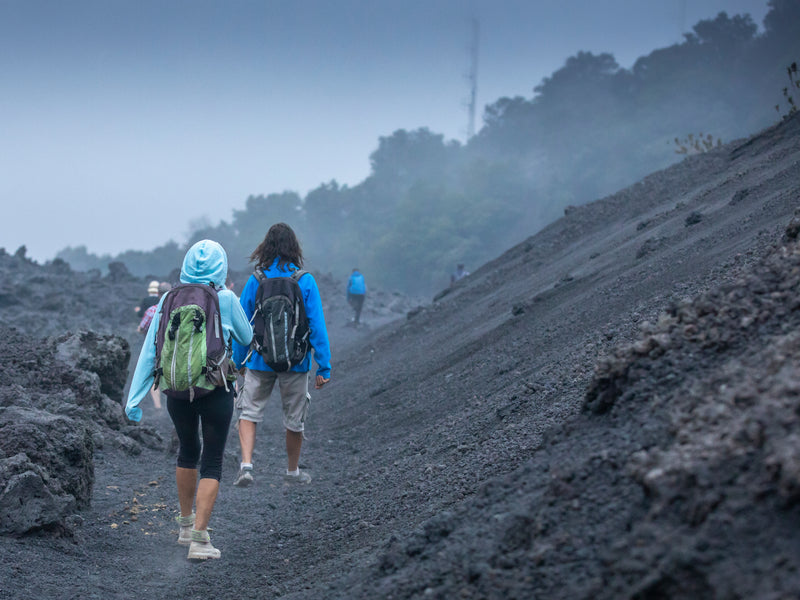 Two hikers with backpacks walking on a volcanic landscape; Pacaya Volcano, Antigua, Guatemala