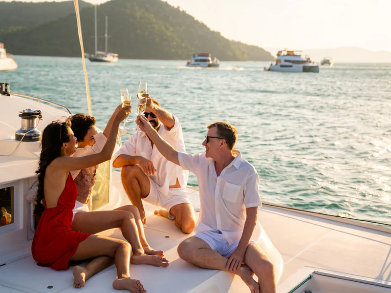 People on a boat celebrating with drinks, surrounded by water and mountains; private catamaran cruise