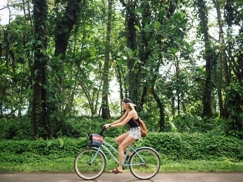 Woman riding a bicycle in a lush green forest; Puerto Viejo, Costa Rica