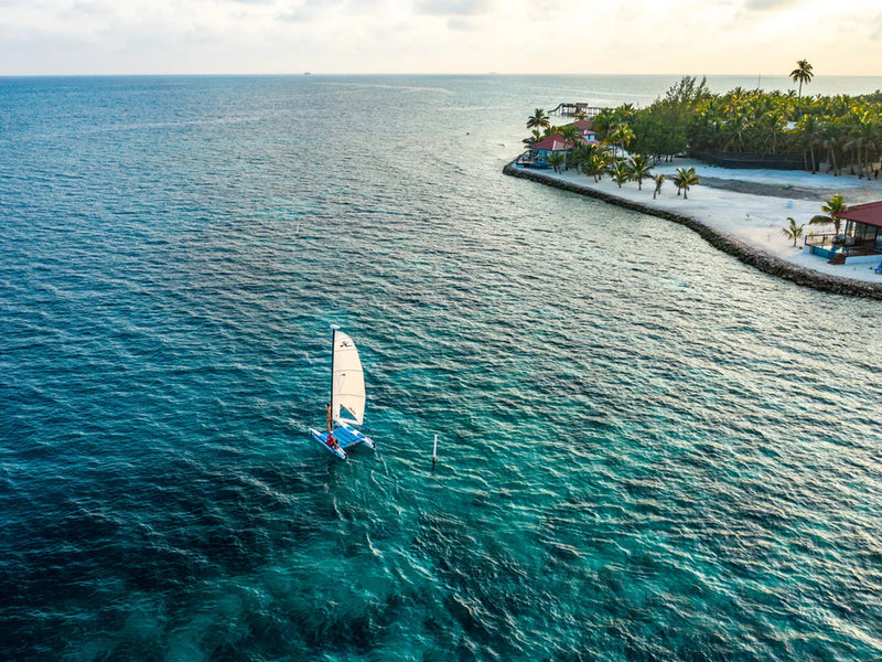 Sailing boat on clear blue water with a tropical island in the background, Ray Caye, Belize