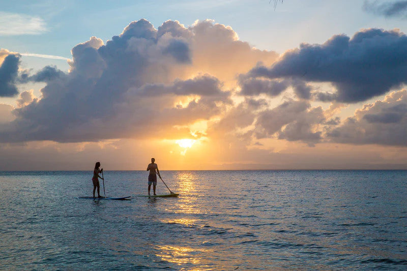 Two people paddleboarding on a calm ocean at sunset with dramatic clouds, Ray Caye, Belize