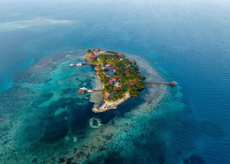Island with houses and docks surrounded by clear blue water; Ray Caye, Belize