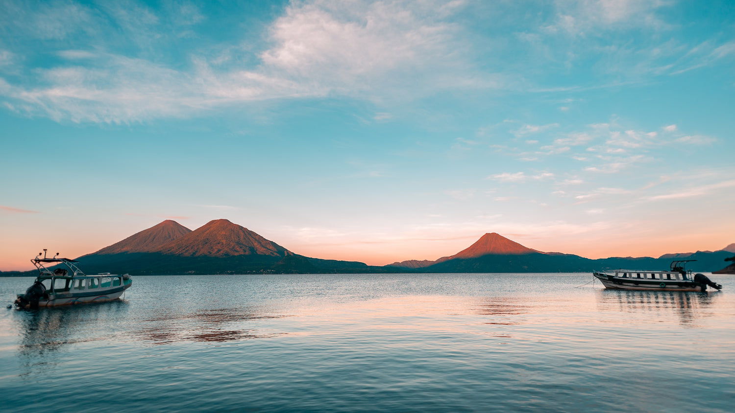 Two boats on a calm lake with mountains in the background during sunset. Lake Atitlan, Guatemala.