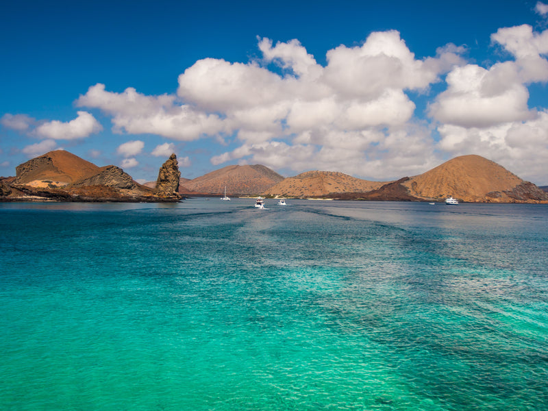 Turquoise waters with rocky islands and a blue sky with clouds; Bartolome Island Galapagos Ecuador