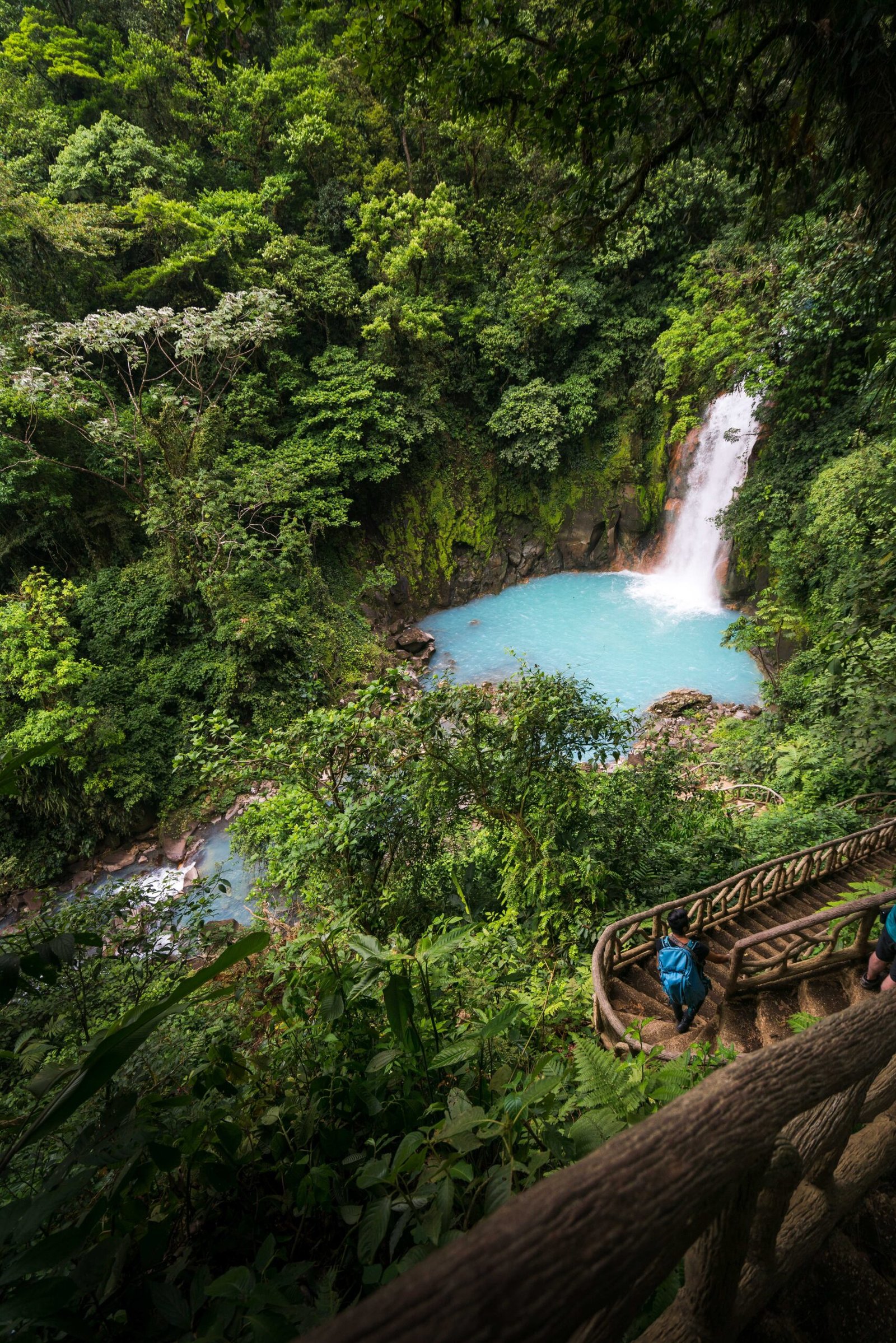 A young man walking down the stairs of the Rio Celeste Waterfall with a blue backpack, Alajuela, Costa Rica.